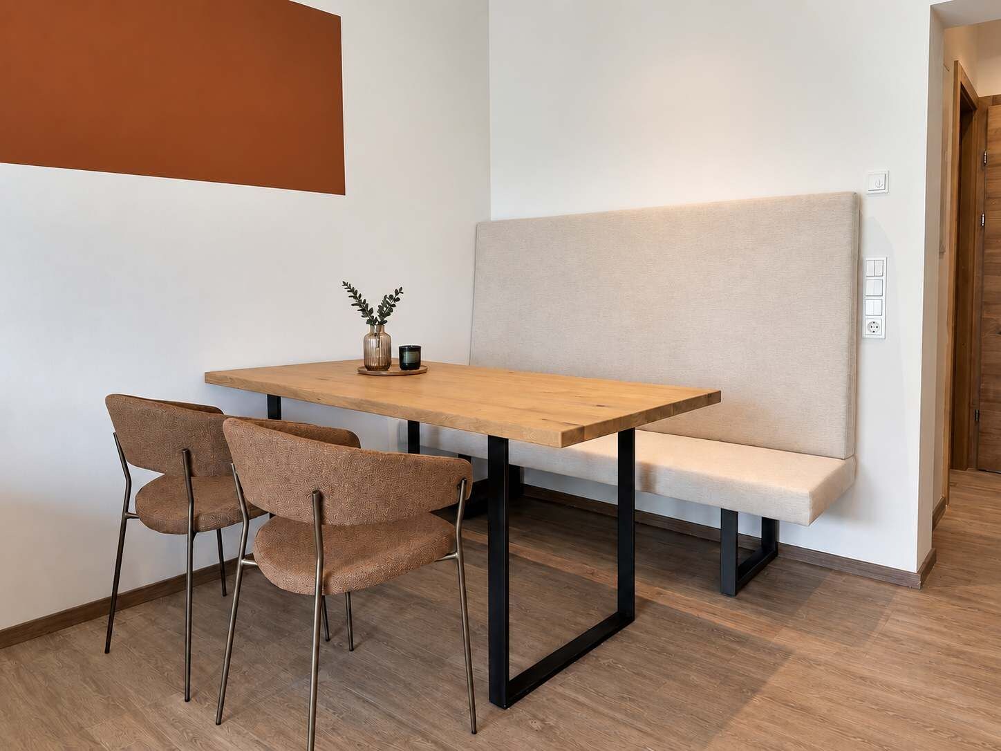 Ein kleiner, moderner Raum mit einem Holztisch, zwei Stühlen, einer Bank und einer Pflanzvase.