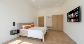 Ein modernes Schlafzimmer mit Bett, Nachttisch, Kleiderschrank und einem an der Wand montierten Fernseher, der Inhalte von Netflix zeigt.