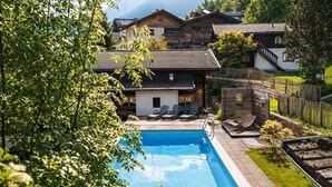 A swimming pool with lounge chairs, surrounded by houses and greenery. - NINA's Chalet – Pool & Sauna Access (Reith im Alpbachtal)