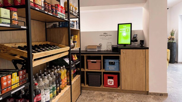 A self-service kiosk area with a digital screen, shelves stocked with snacks and beverages, and a wooden counter. - BASE Achensee Soul N°32 (Achenkirch)