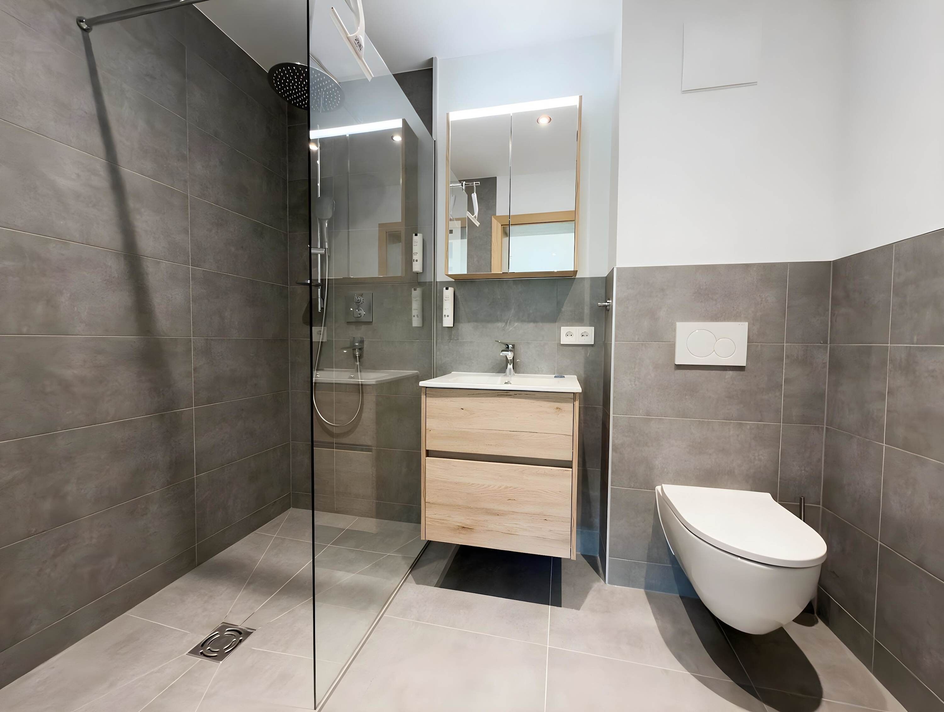 Ein modernes Badezimmer mit einer begehbaren Glasdusche, einem Holzbadezimmerflansch, einer weißen Toilette und einem großen Spiegel.
