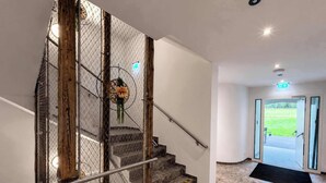 A staircase with a metal railing, a wooden post, and a flower decoration. There is a door leading to an outdoor area. - BASE Achensee Soul N°32 (Achenkirch)