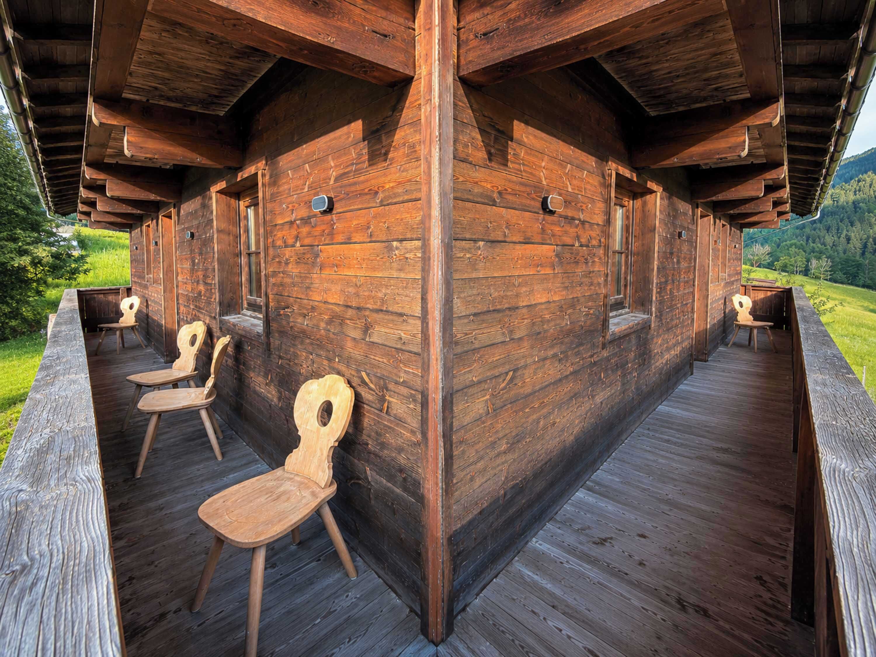 A wooden cabin with a deck, two wooden chairs, and a view of a green landscape.