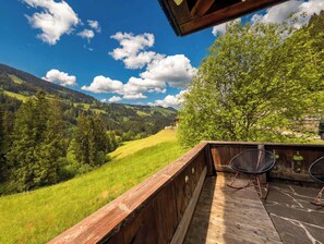 Eine Holzterrasse mit Blick auf ein grünes Tal und Berge.