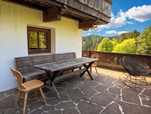 A wooden bench, a table, and two chairs on a stone patio with a view of a forested mountain range. - CHALET Naschberg - 5 BR, Terrace & Mountain View (Scheffach)