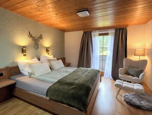 Un dormitorio con techo de madera, cama con ropa de cama blanca, manta verde, una silla y una lámpara.