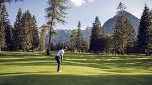 Une personne jouant au golf sur un parcours bien entretenu, avec de grands arbres et des montagnes en arrière-plan.
