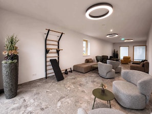 Eine moderne Lounge mit Steinboden, grauen Sofas, einer Holz-Kletterwand und einer großen Topfpflanze.