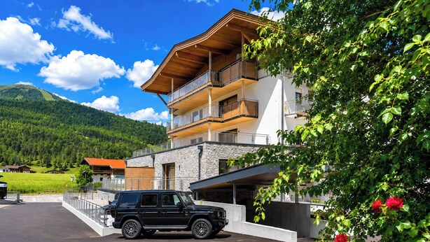 Un bâtiment moderne avec une façade en pierre, de nombreux balcons et un VUS garé devant.