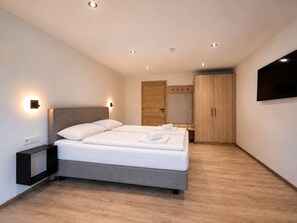 Een moderne hotelkamer met een tweepersoonsbed, nachtkastjes, een kledingkast en een aan de muur bevestigde televisie.