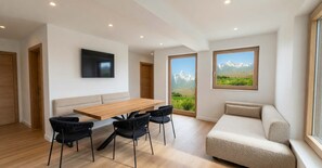 Ein modernes Wohnzimmer mit einem Holzesstisch, schwarzen Stühlen, einem beigen Sofa und einem an der Wand befestigten Fernseher.
