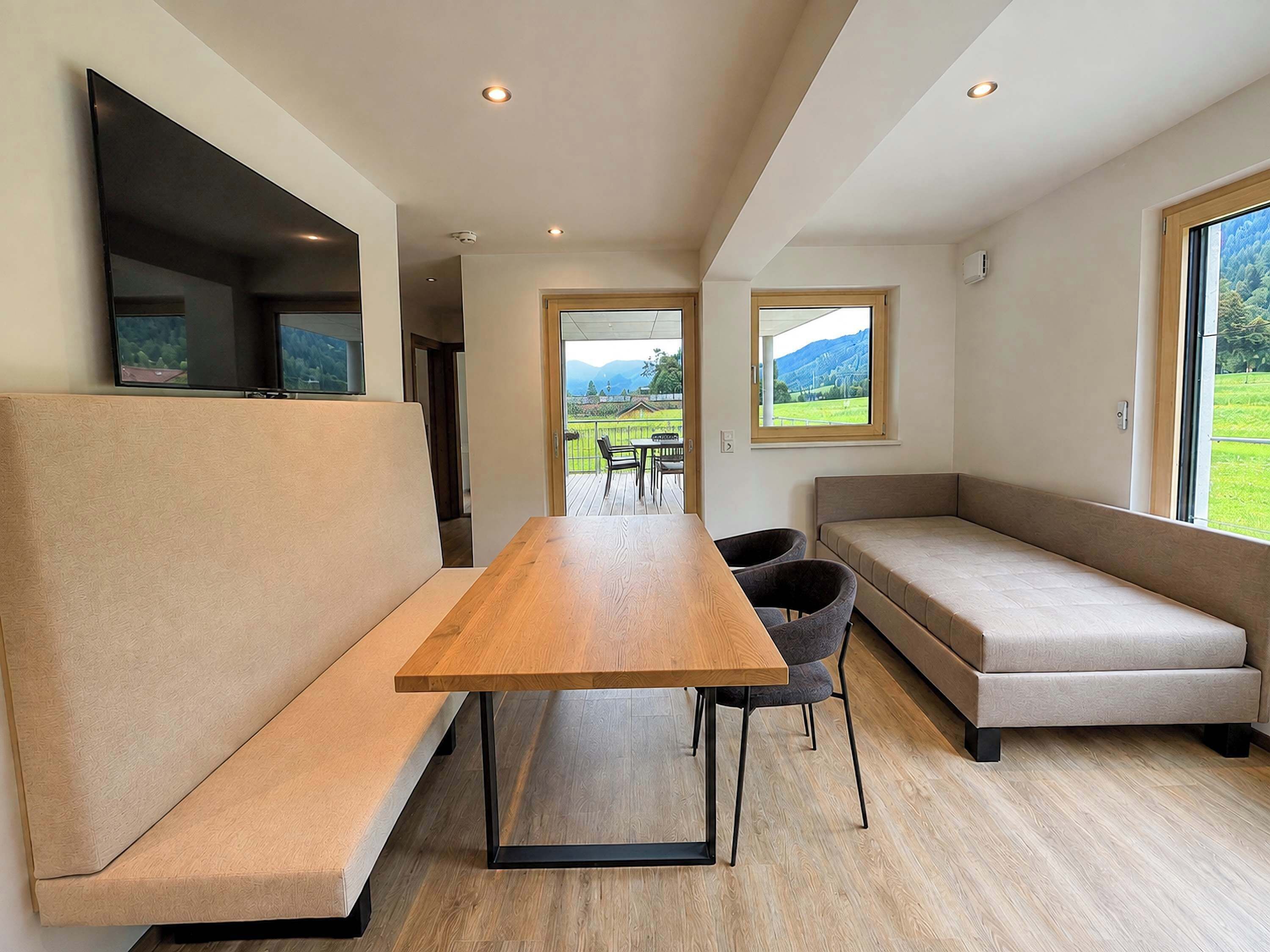 Un intérieur moderne avec une table à manger en bois, des sièges confortables et de grandes fenêtres offrant une vue sur un paysage verdoyant.