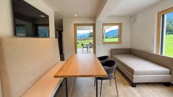 Un intérieur moderne avec une table à manger en bois, des sièges confortables et de grandes fenêtres offrant une vue sur un paysage verdoyant.
