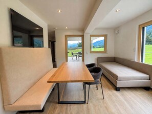 Een modern interieur met een houten eettafel, comfortabele zittingen en grote ramen met uitzicht op een groen landschap.