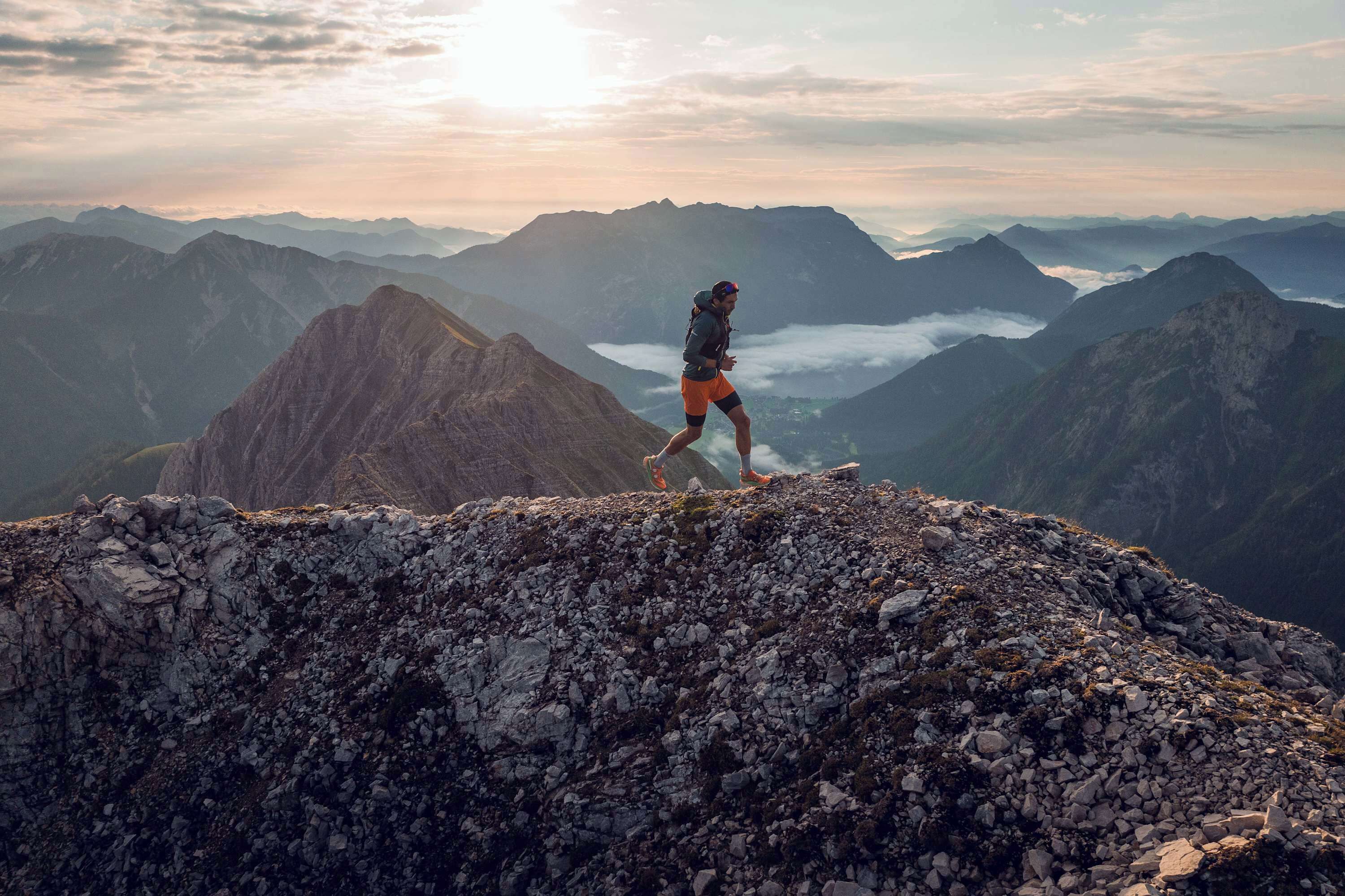 A person hiking on a rocky mountain peak with a view of multiple mountain ranges in the background.