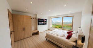 A bedroom with a large window, a bed, a wardrobe, and a mounted TV displaying a Netflix interface. - BASE Achensee Soul No1 – Private sauna (Achenkirch)