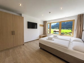 Quarto com uma cama grande, televisão fixada na parede e janela com vista para as montanhas.