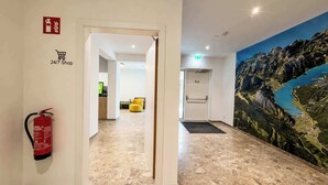 Een hotel lobby met een brandblusser, een bord voor een winkel, open 24 uur per dag, en een muurschildering van een berglandschap.