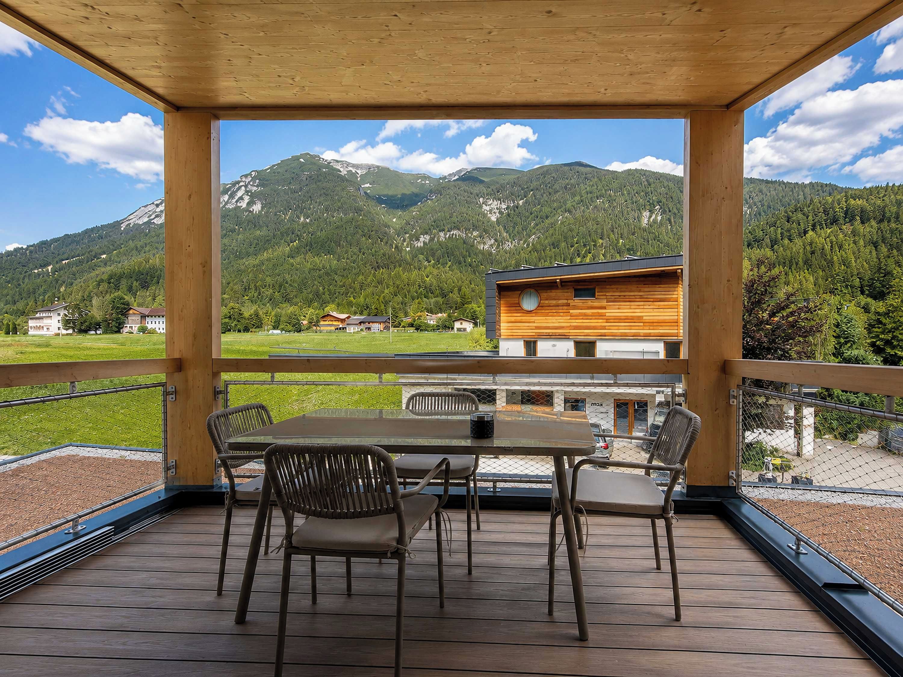 A wooden deck with a table and chairs, overlooking a mountain landscape.