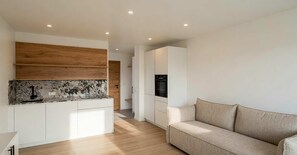 A modern kitchen with white cabinets, a wooden accent wall, and a marble backsplash. - BASE Achensee Energy No5 – Terrace with a daybed (Achenkirch)