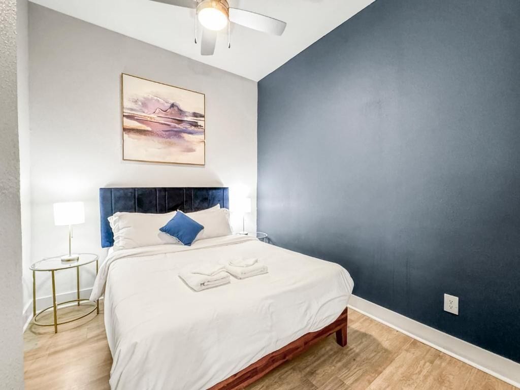 Une chambre à coucher comprenant un lit, une tête de lit, un tableau accroché au mur, une table de chevet et une lampe.