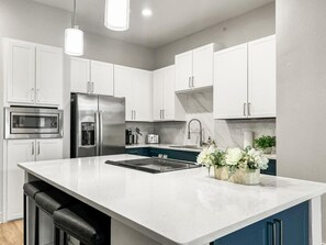 A modern kitchen with white cabinets, a stainless steel refrigerator, a built-in oven, and a large island with a sink. - Apartmint at Deep Ellum Dallas (Dallas)