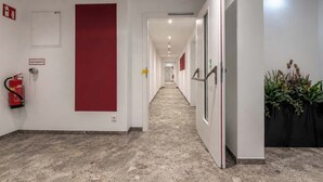Corredor de hotel com extintor de incêndio, sinalização de saída de emergência vermelha e sinalização de saída de emergência verde.