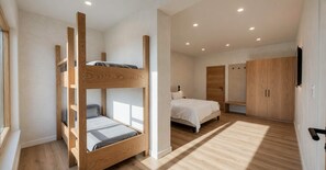 Ein Zimmer mit Etagenbetten, einem Einzelbett, Holzboden, einem Kleiderschrank und einem Fernseher.