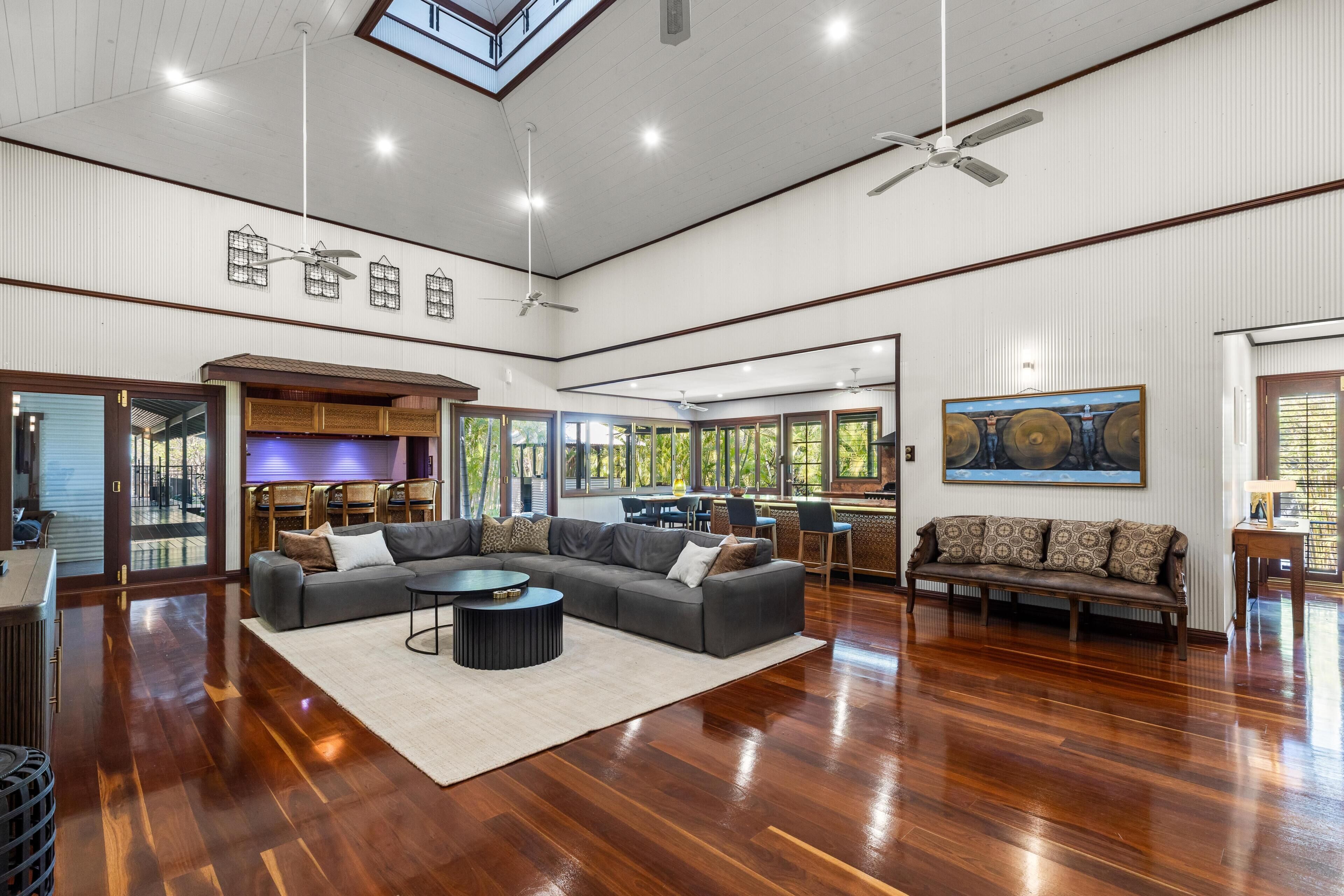 Spacious living room with polished hardwood floors, vaulted ceiling, gray sectional, and large windows overlooking greenery.
