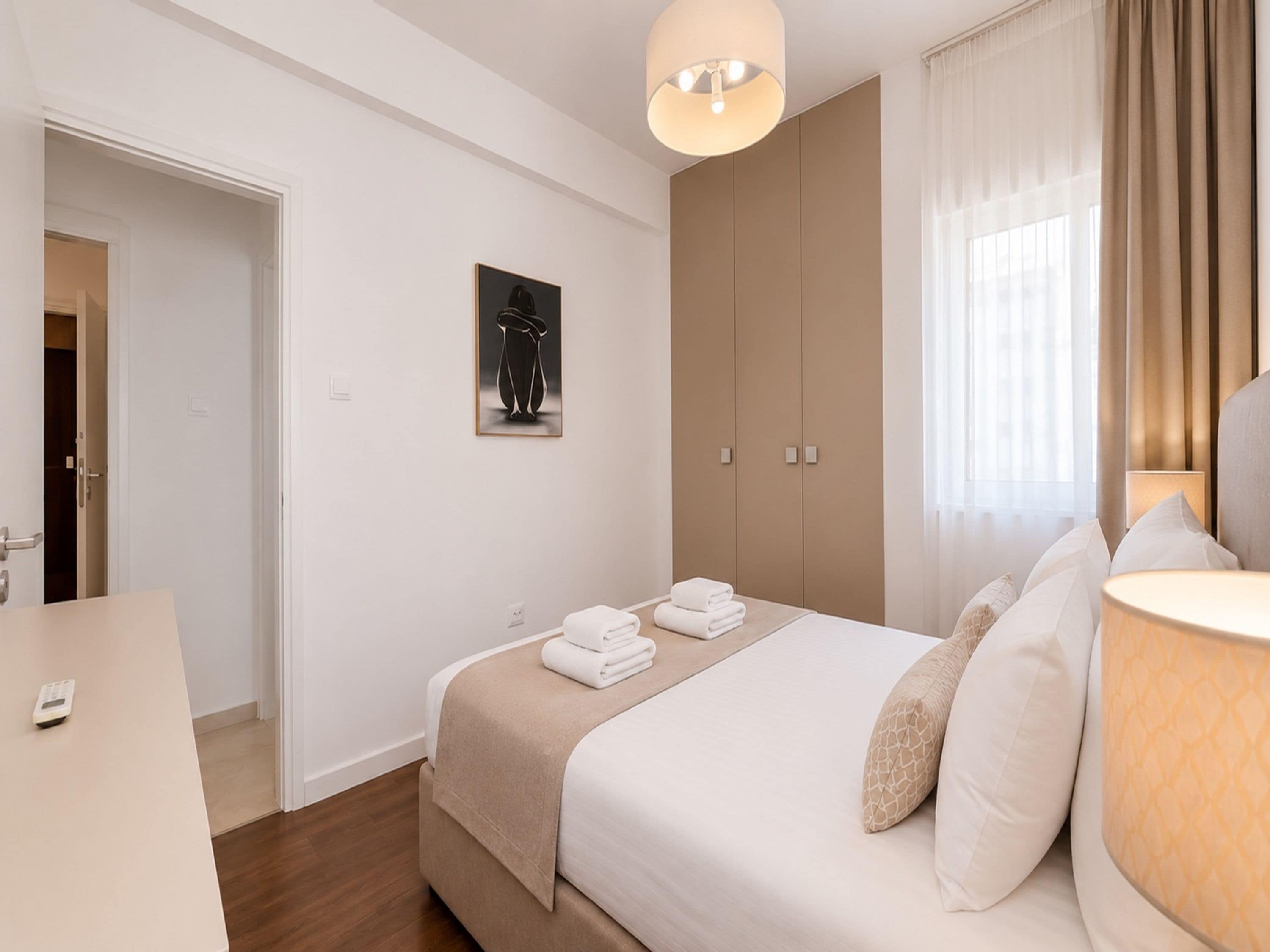 A hotel room with a bed, a bedside table, a wardrobe, and a window with curtains.