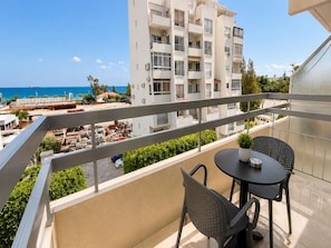 Ein Balkon mit Tisch und Stühlen, mit Blick auf ein Gebäude und das Meer.