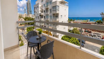 Un balcón con dos sillas y una mesa, con vistas a un paisaje urbano con edificios y al mar.