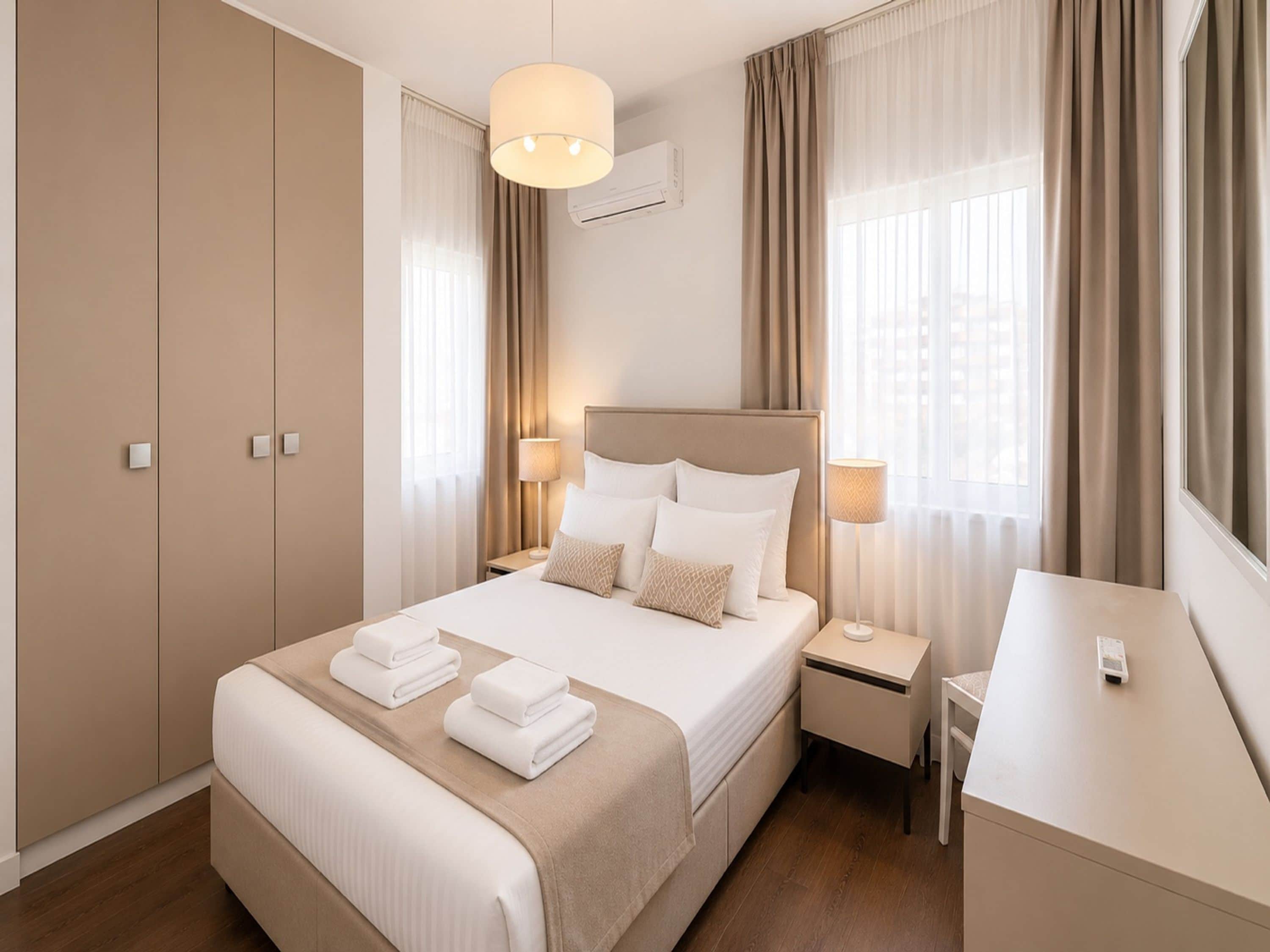 Una habitación de hotel con cama, lámparas de noche, escritorio y armario.