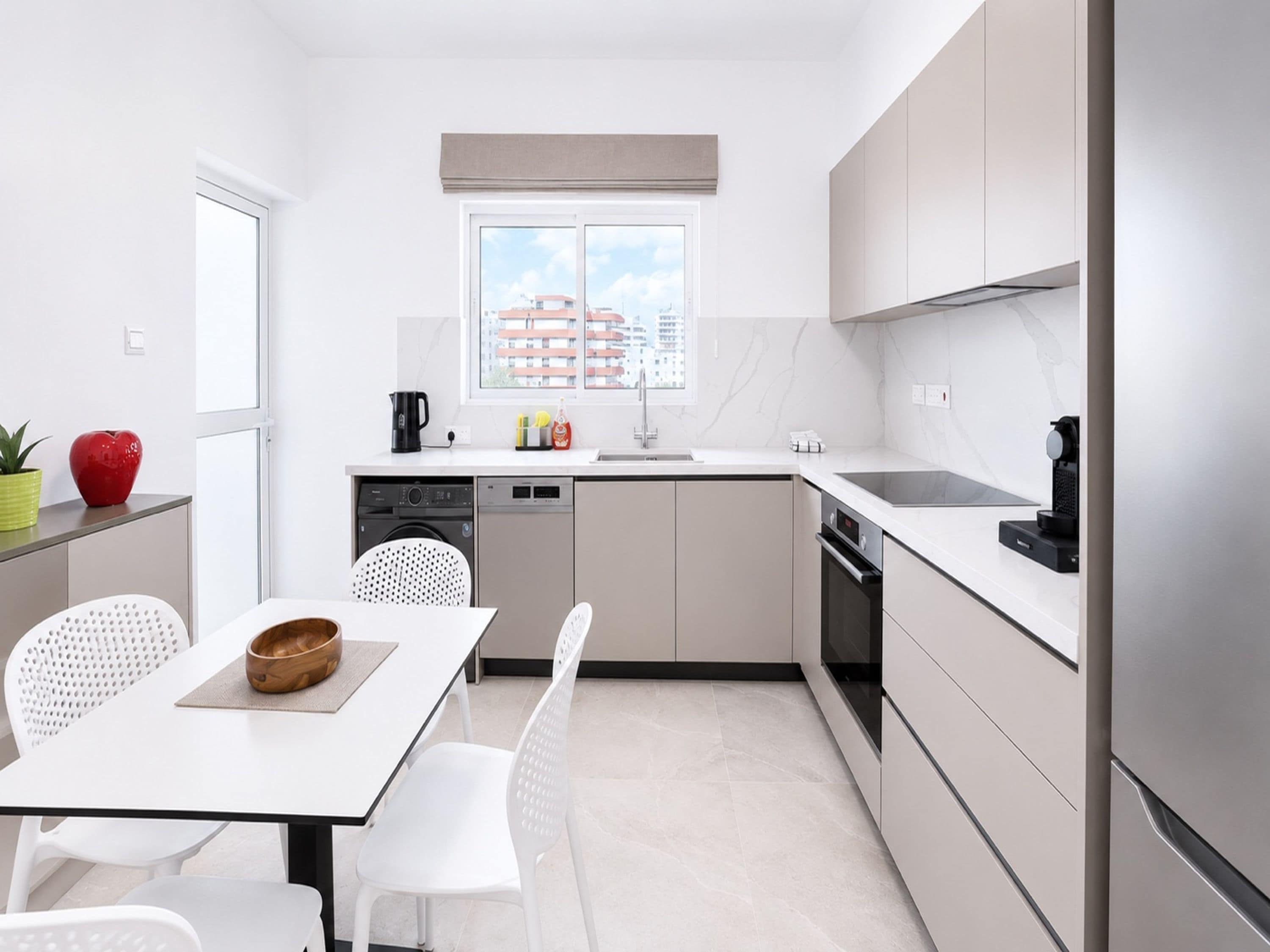 A modern kitchen with a dining area, white cabinetry, a window with a city view, and a small table with chairs.