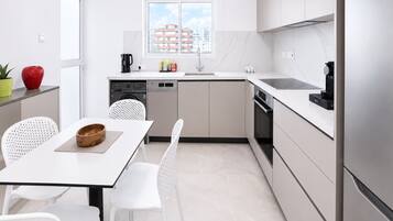 A modern kitchen with a dining area, white cabinetry, a window with a city view, and a small table with chairs.