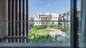 A balcony with a view of a modern apartment complex, a grassy area, and a pool. - Sodic Eastown  Panoramic EDNC View + Monorail (Cairo Governorate)