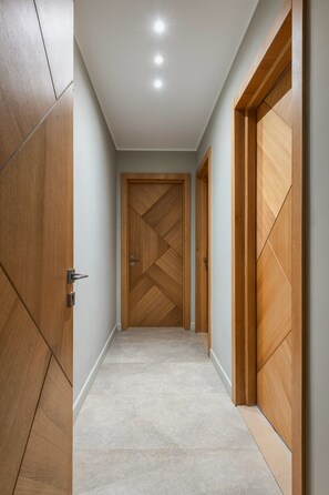 A hallway with wooden doors, a light-colored floor, and recessed ceiling lights. - Apartment in Cairo 3BR with AC (Cairo Governorate)