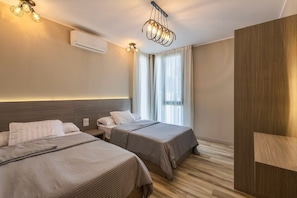 A hotel room with two beds, a wooden wardrobe, a ceiling light fixture, and a window with curtains. - Apartment in Cairo 3BR with AC (Cairo Governorate)