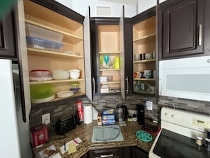 A kitchen with open cabinets, a microwave, a stove, and various kitchen items on the counter.