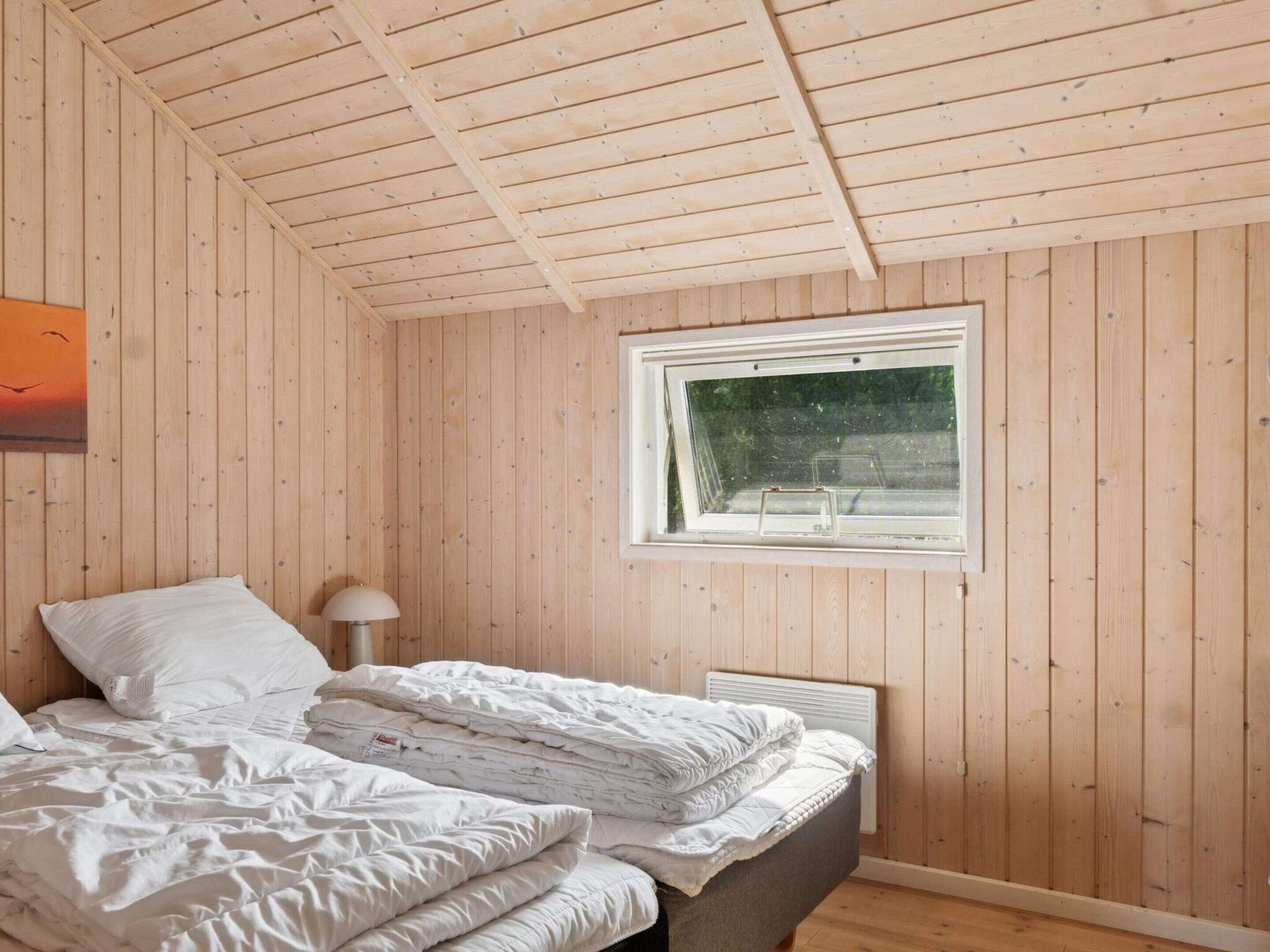 A bedroom with wooden walls, a bed with white bedding, a window, and a nightstand with a lamp.