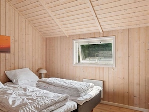Ein Schlafzimmer mit Holzwänden, einem Bett mit weißer Bettwäsche, einem Fenster und einem Nachttisch mit Lampe.