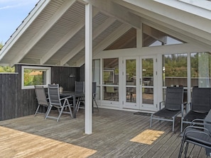 A covered patio with a table and chairs, a wooden deck, and a view of the surrounding area. - 4 Star Holiday Home in Rodby (Rodby)