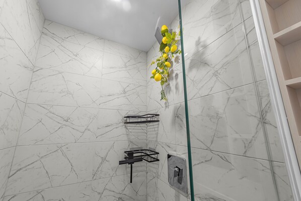 A bathroom with white marble walls, a glass shower enclosure, and a black towel rack.