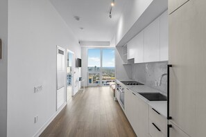 A modern kitchen with white cabinets, a large window, and a view of the city. - Saint Suites - Penthouse 2Bed+2Bath High Rise Condo (Toronto)