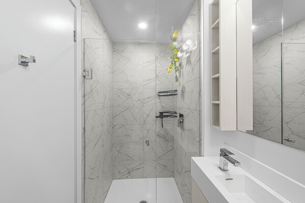 Un baño moderno con ducha, tocador con espejo y pared de mármol.