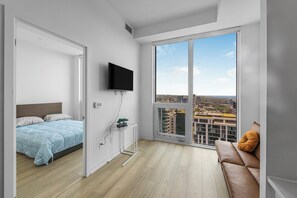 A modern bedroom with a bed, a TV, a small table with a plant, and a sofa with a cushion. - Saint Suites - Penthouse 2Bed+2Bath High Rise Condo (Toronto)