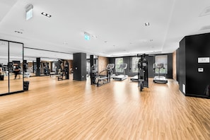 A gym with exercise equipment, wooden flooring, and a large mirror.