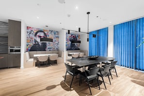 A modern dining area with a black table and chairs, a large mural on the wall, and a blue curtain on the window.