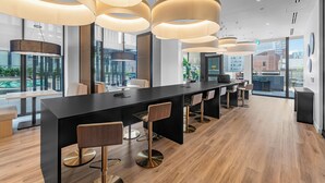 A modern bar area with a long counter, multiple bar stools, and pendant lighting. - Saint Suites - Penthouse 2Bed+2Bath High Rise Condo (Toronto)