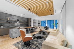 A modern kitchen with marble countertops, a wooden ceiling, and a dining area with a blue curtain backdrop.